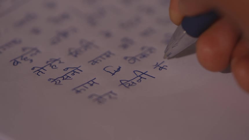 Hand writes on a paper with hindi script text using a blue pen
