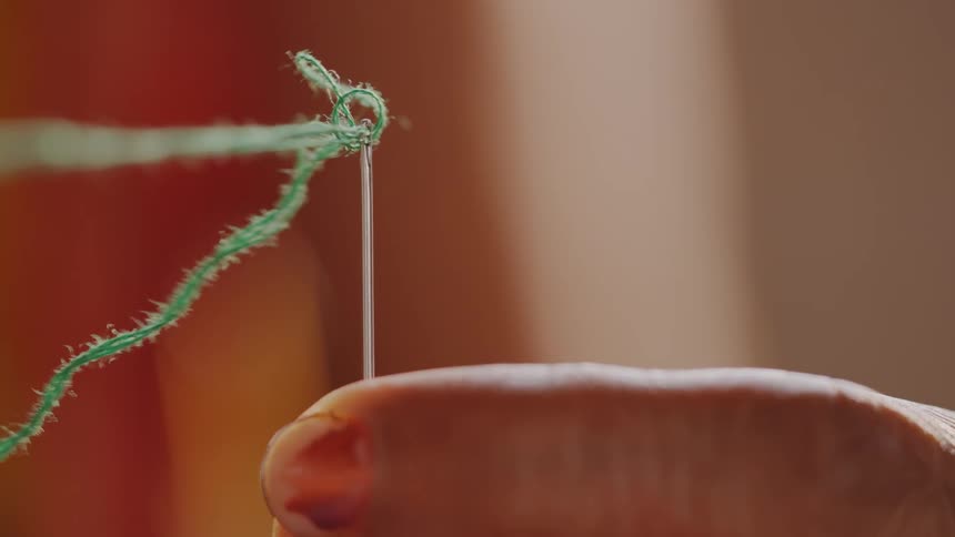 A persons finger threading a needle with green thread