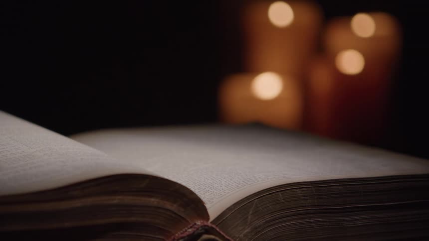 Old book being flipped through with candles blurred in the background
