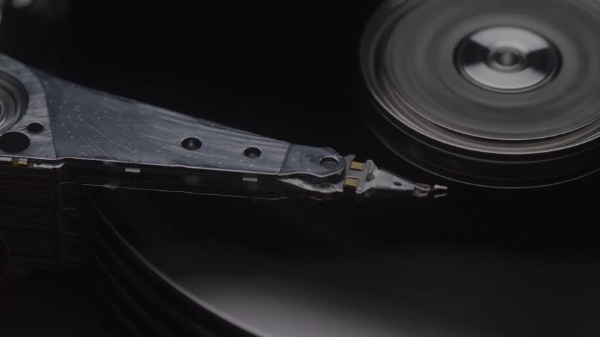 A close view of an open hard drive shows the silver read write head moving back and forth across the spinning black platters