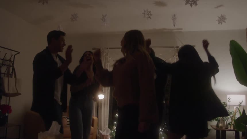 Friends dance around a lit christmas tree in a dim living room