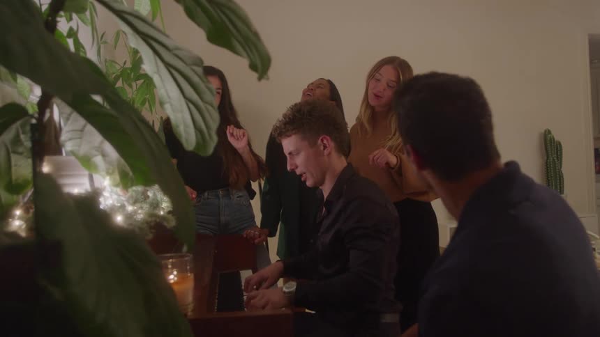 Friends sing around a piano at a cozy house gathering