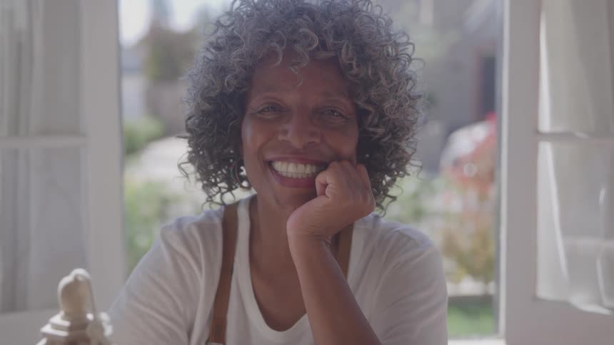 The video shows a closeup of a middleaged woman with short gray curly hair she is smiling warmly at the camera resting her chin on her hand