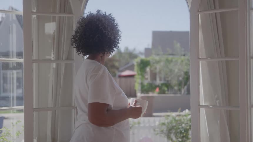 The woman looks out the window with a cup of coffee