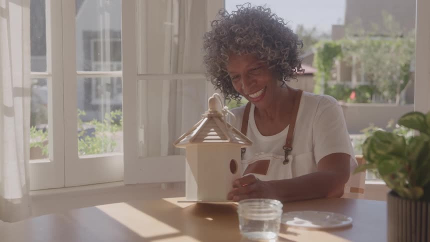 Smiling woman looks at a wooden birdhouse on a sunlit table