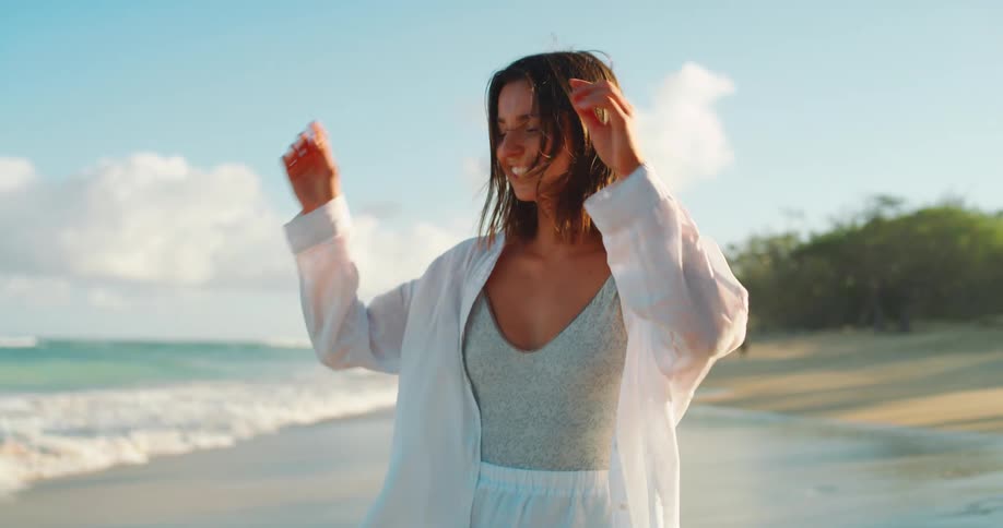 Young woman smiles as she walks on the beach as waves roll into shore