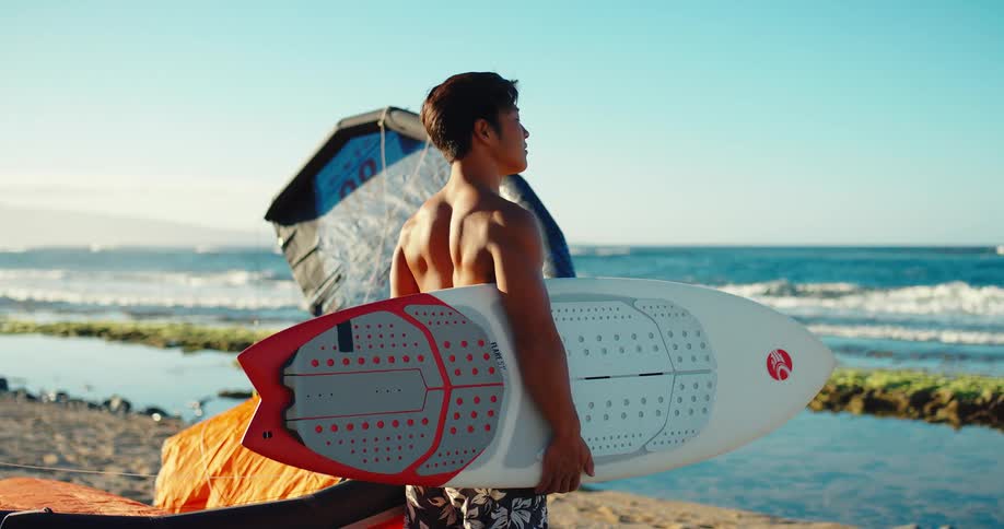 Man holds a surfboard on the sand near the sea on a sunny day