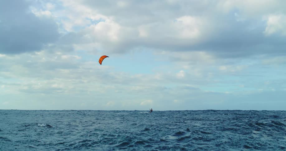 Kitesurfer glides over the open sea with an orange kite in the background