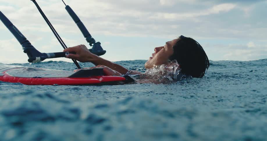 Based on the images from the video a man is seen in the ocean with a kiteboarding rig partially visible his head is above the water as he looks up at the sky which has some clouds