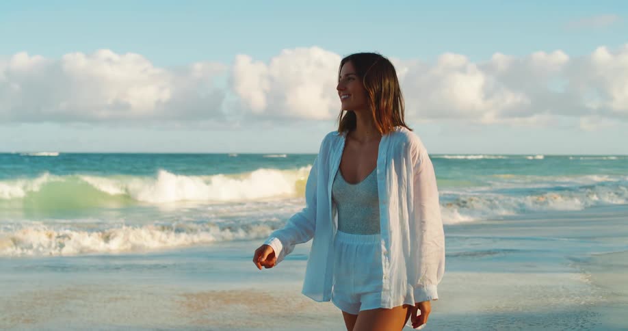Young woman walking on the beach looks around and smiles as waves roll into shore
