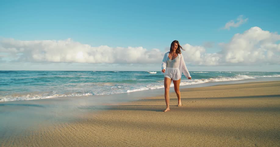 A woman strolls barefoot along a sunny beach