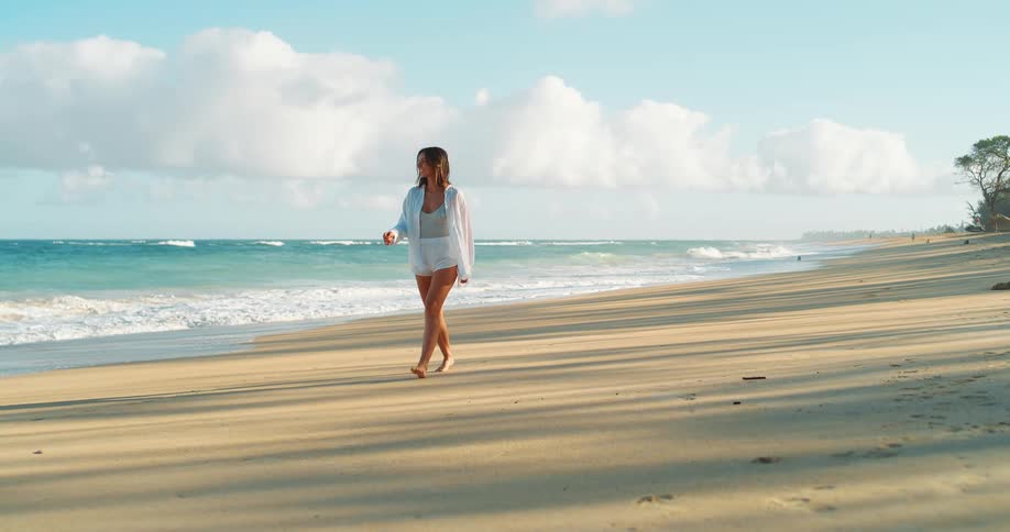 Woman walks barefoot along the beach under the soft morning light
