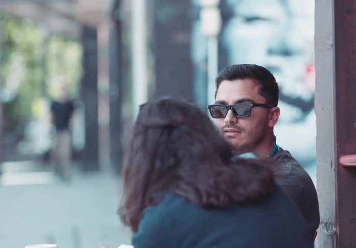 A man wearing sunglasses talking to a woman who is in front of him