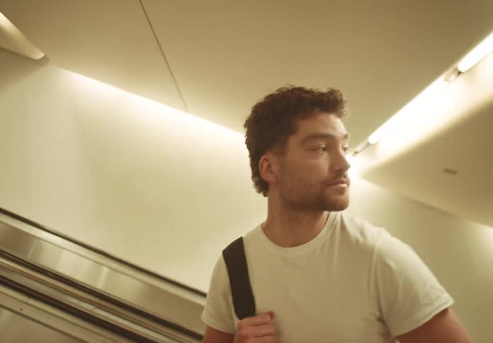 Man in a white tshirt rides the escalator while looking upward