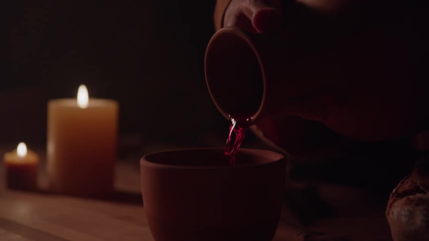 Wine being poured into a clay cup beside lit candles