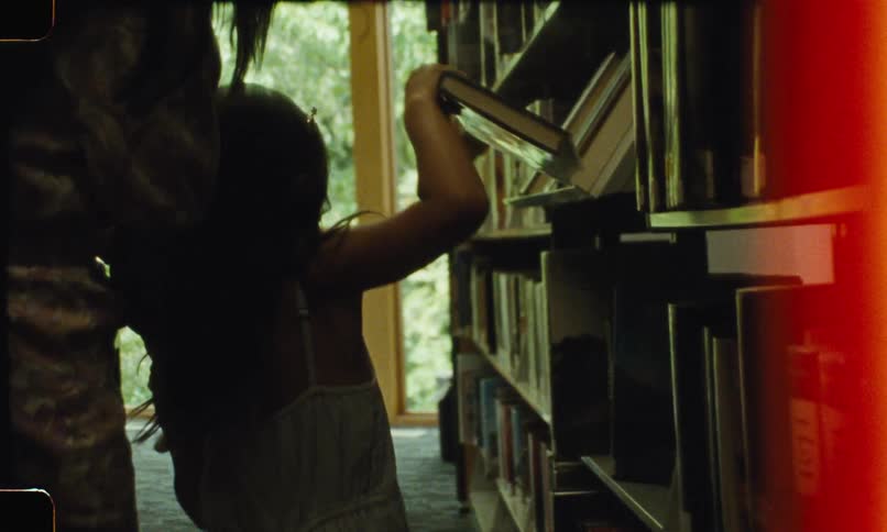 A child standing in a library reaching up to a high shelf to take a book