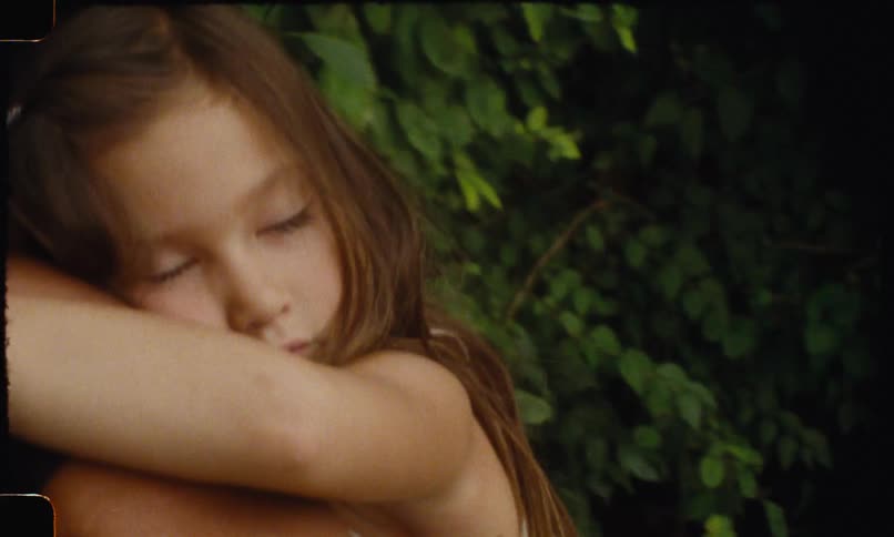 A sleepy child rests in someones arms with a vintage film look
