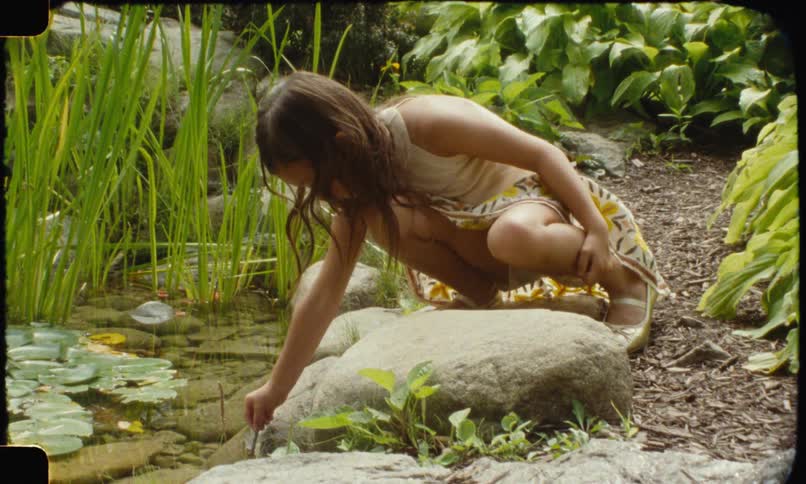 Girl crouching by a pond touches the water with her hand