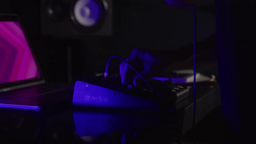 A person adjusts controls on an audio mixer in a dimly lit studio
