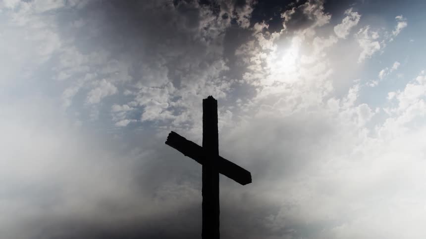 Wooden cross in silhouette against a cloudy sky lit by the sun