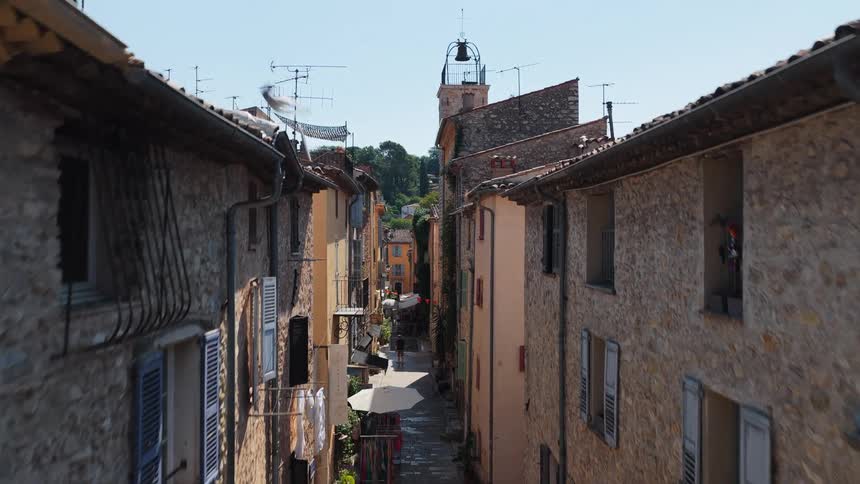 Narrow alleys between stone houses with a tower and bell in the background