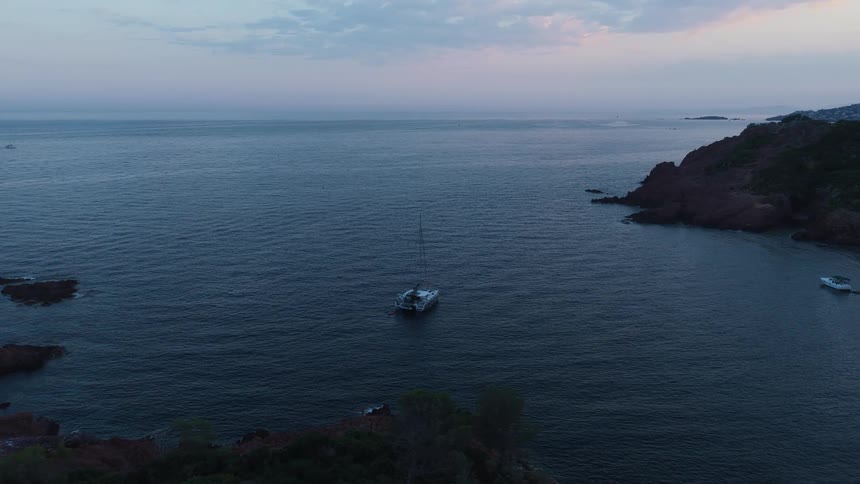 Boats sail on the water with mountains and rocks along the coast under a cloudy sky