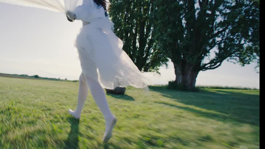 Person runs through a sunny field with flowing white fabric
