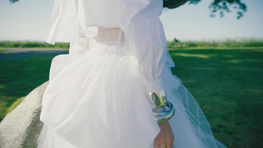 A woman walks around a rock in a white dress