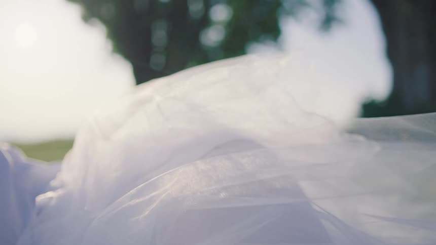 Based on the images from the video a closeup shot shows a persons hair and shoulder as they are covered by a thin white cloth the scene is outdoors on a bright sunny day with green grass in the background