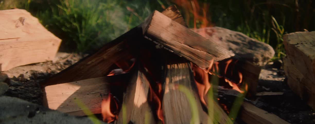 A small campfire burning with stacked wooden logs outdoors