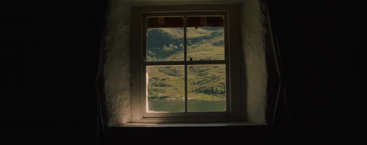 Small window looks out onto a lake and a mountain slope in the rural countryside