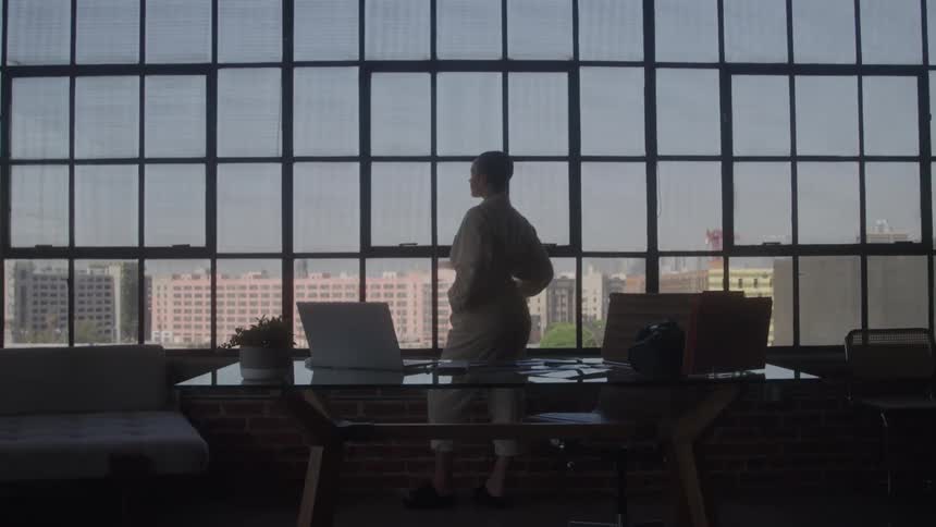 Person stands by large office windows looking out over the city