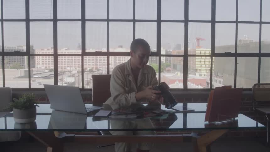 Person sitting at a glass desk examines a camera in an office setting