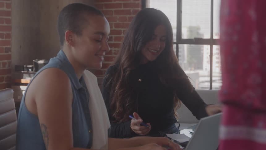 Two colleagues smile and collaborate at a laptop in a loft office
