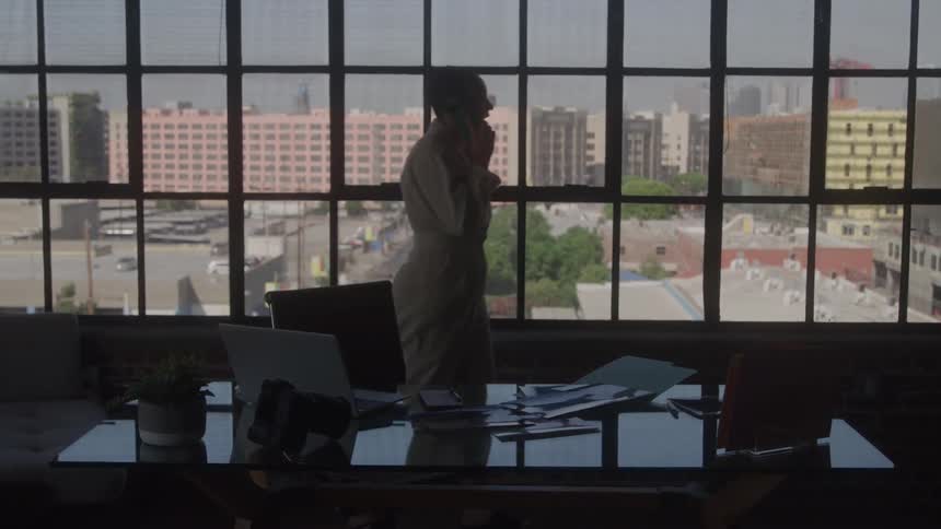 An office worker talks on the phone by large loft windows overlooking the city
