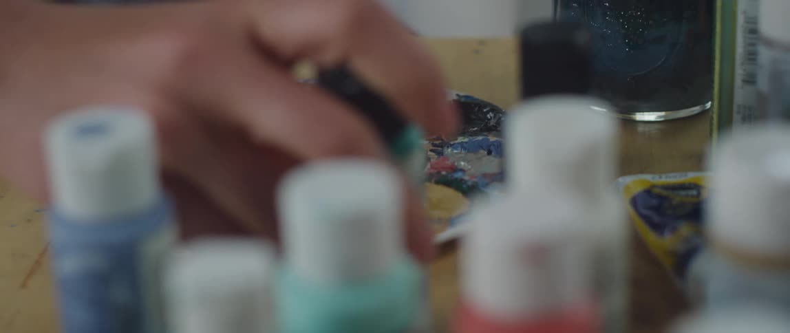 The artist puts a paint bottle down