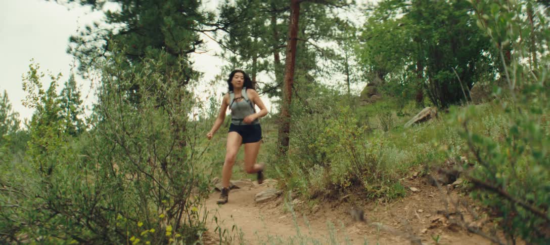 Woman runs along a trail surrounded by forest vegetation