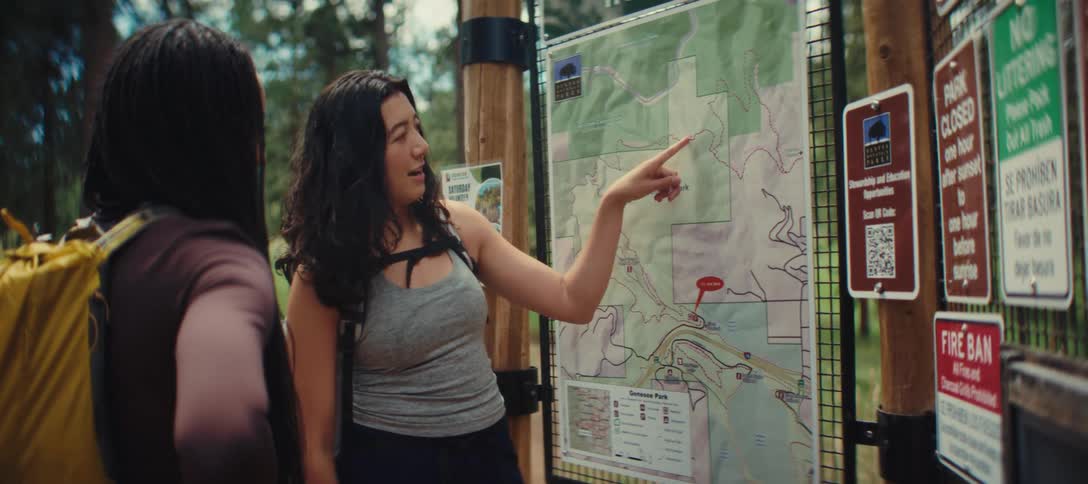 Two hikers examine a trail map at the entrance of a forest