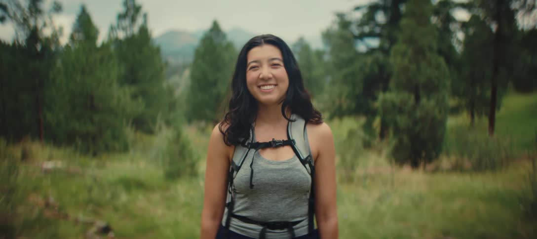 Smiling woman with a hiking backpack in a green mountain area