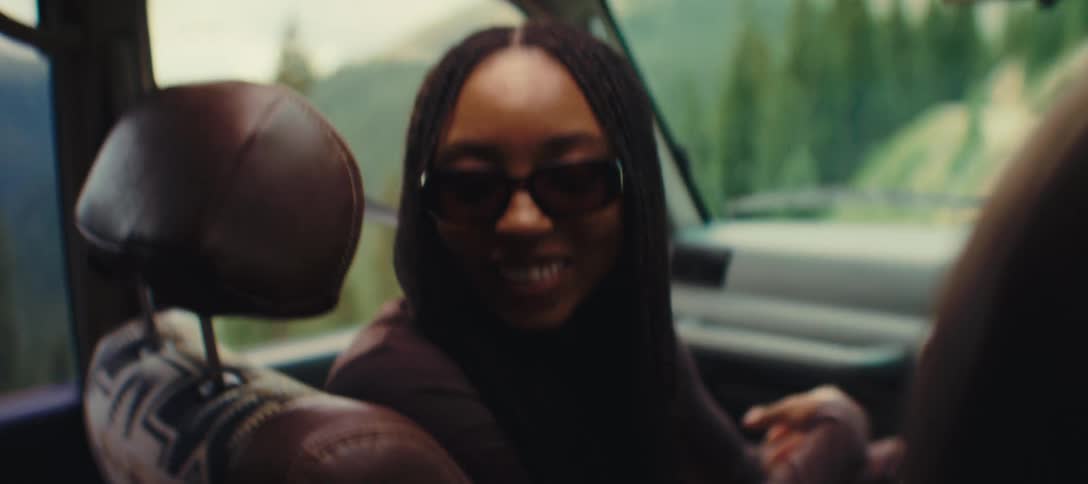 Two women laughing and talking inside a car one in the backseat and one in the front turning back