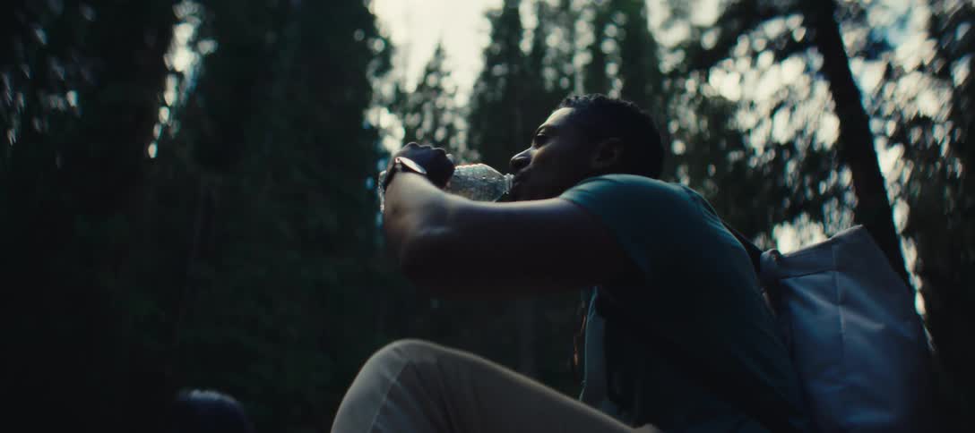 A man drinks water while hiking in a dense forest