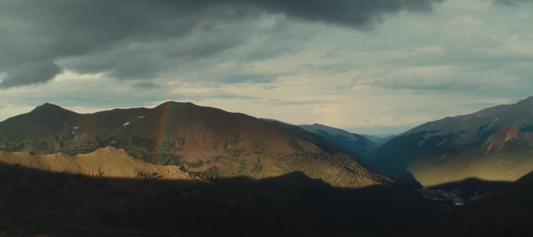 Rainbow appears between mountains under a partly cloudy sky