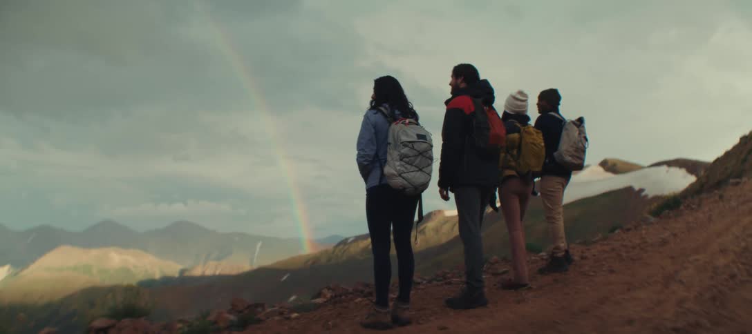 Hikers are stopped and looking at a rainbow in the distance
