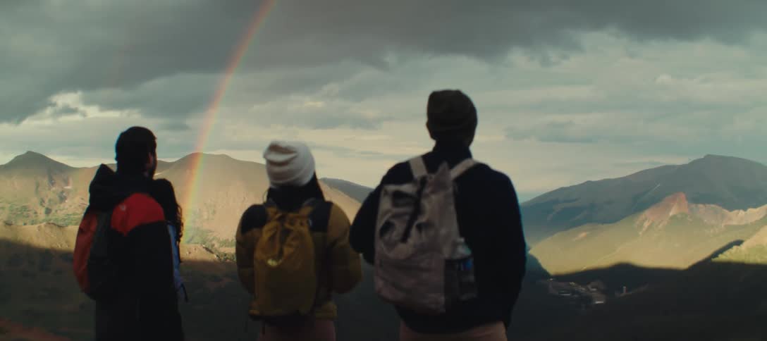 Group of hikers watches a rainbow over the mountains