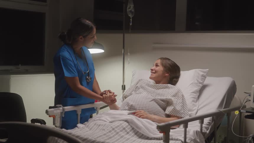 Nurse holds the hand of a smiling patient lying in a hospital bed