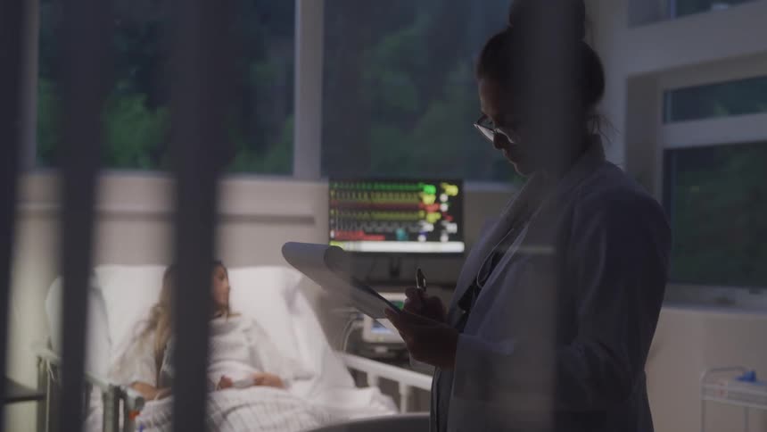 Doctor takes notes while a patient rests in a hospital bed