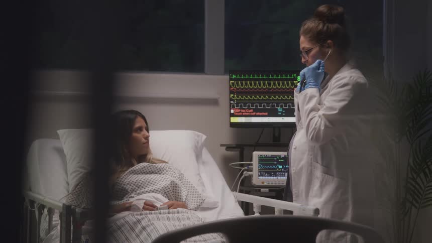 A doctor checks a patient in a hospital bed beside monitors