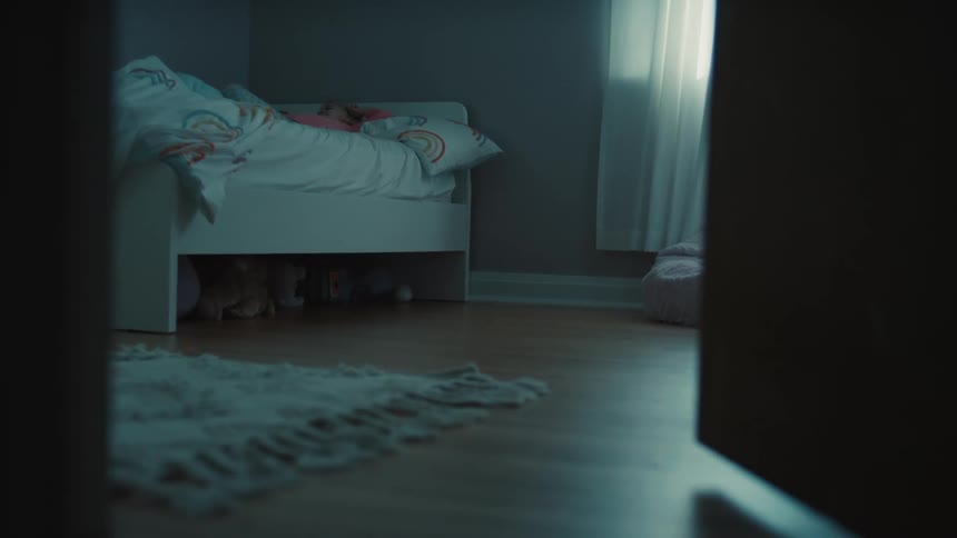 A child sleeping peacefully in a white bed in a dim room with the camera peeking in through a partially open door