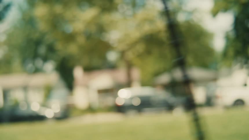 A woman wearing a white t shirt and a gray sun hat is pushing a little girl with blonde hair in a ponytail who is swinging on a tire swing in a backyard