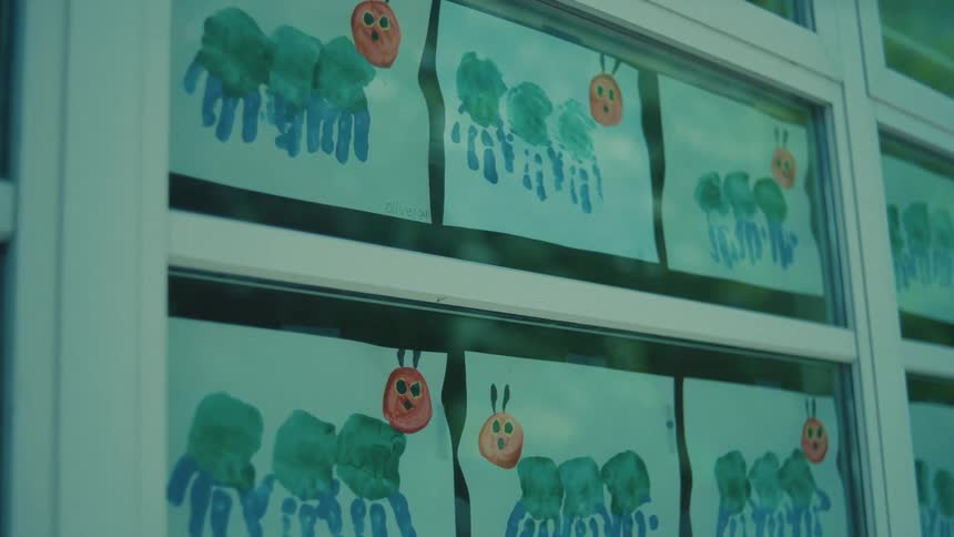 A kids painting of three green and blue palm fingers with a round character beside them displayed in several copies on a window glass